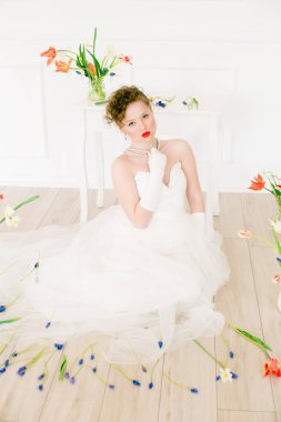 Beyaz elbiseli çekici bir gelin, lalelerle süslenmiş hafif bir bahar stüdyosunda. Güzellik ve Moda