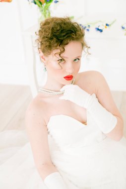Beyaz elbiseli çekici bir gelin, lalelerle süslenmiş hafif bir bahar stüdyosunda. Güzellik ve Moda