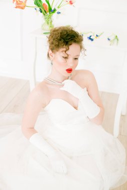 Beyaz elbiseli çekici bir gelin, lalelerle süslenmiş hafif bir bahar stüdyosunda. Güzellik ve Moda