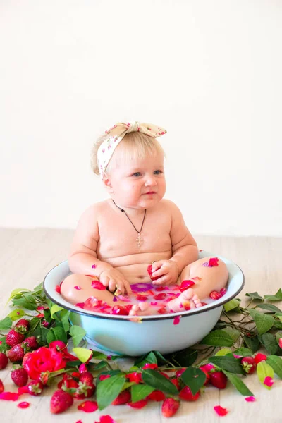 かわいい赤ちゃんの女の子はピンクの花びらとイチゴと流域に座っています — ストック写真