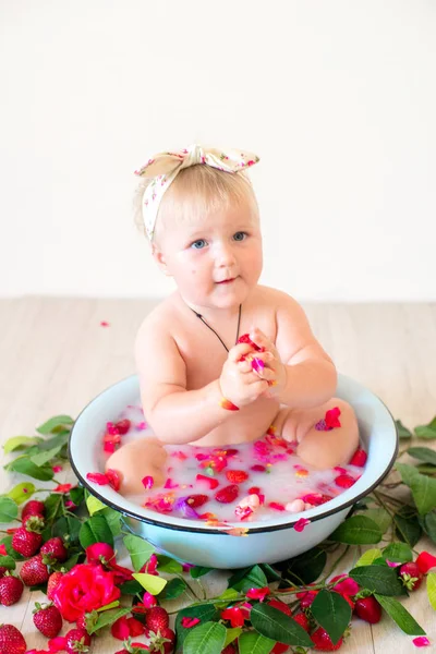 かわいい赤ちゃんの女の子はピンクの花びらとイチゴと流域に座っています — ストック写真