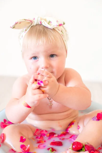 かわいい赤ちゃんの女の子はピンクの花びらとイチゴと流域に座っています — ストック写真