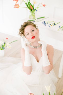 Beyaz elbiseli çekici bir gelin, lalelerle süslenmiş hafif bir bahar stüdyosunda. Güzellik ve Moda