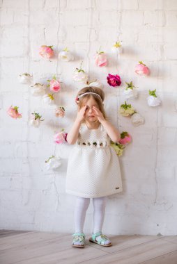Bahar ışığı stüdyosunda çiçeklerle süslenmiş güzel beyaz elbiseli küçük tatlı kız.
