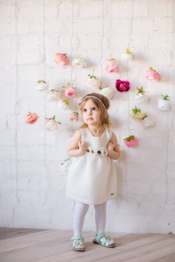 Bahar ışığı stüdyosunda çiçeklerle süslenmiş güzel beyaz elbiseli küçük tatlı kız.