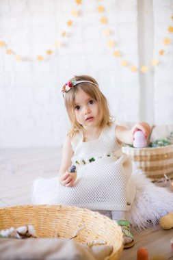 Beyaz elbiseli küçük tatlı kız oyuncaklar ve çelenklerle süslenmiş parlak bir çocuk odasında oynuyor..