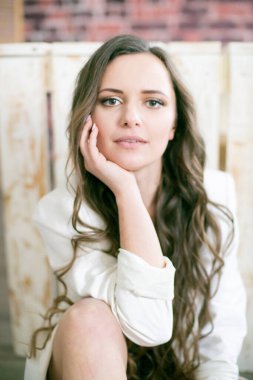 Uzun kıvırcık saçlı, dantelli siyah ceketli ve beyaz, şık ceketli çekici bir kadın stüdyoda yerde oturuyor.