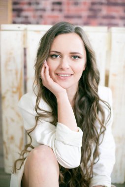 Uzun kıvırcık saçlı, dantelli siyah ceketli ve beyaz, şık ceketli çekici bir kadın stüdyoda yerde oturuyor.