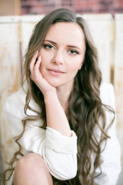 Uzun kıvırcık saçlı, dantelli siyah ceketli ve beyaz, şık ceketli çekici bir kadın stüdyoda yerde oturuyor.