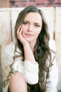 Uzun kıvırcık saçlı, dantelli siyah ceketli ve beyaz, şık ceketli çekici bir kadın stüdyoda yerde oturuyor.