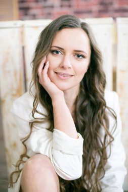 Uzun kıvırcık saçlı, dantelli siyah ceketli ve beyaz, şık ceketli çekici bir kadın stüdyoda yerde oturuyor.