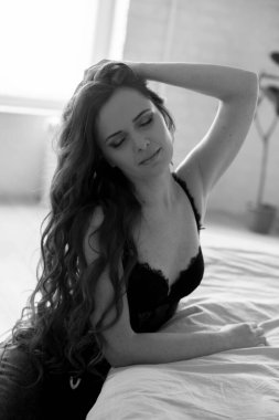 Uzun kıvırcık saçlı, kot pantolonlu, yatakta dantelli siyah tişörtlü çekici bir kadın.