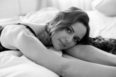 Uzun kıvırcık saçlı, kot pantolonlu, yatakta dantelli siyah tişörtlü çekici bir kadın.