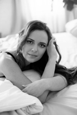 Uzun kıvırcık saçlı, kot pantolonlu, yatakta dantelli siyah tişörtlü çekici bir kadın.