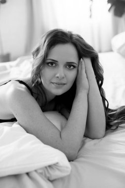 Uzun kıvırcık saçlı, kot pantolonlu, yatakta dantelli siyah tişörtlü çekici bir kadın.