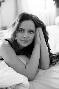 Uzun kıvırcık saçlı, kot pantolonlu, yatakta dantelli siyah tişörtlü çekici bir kadın.