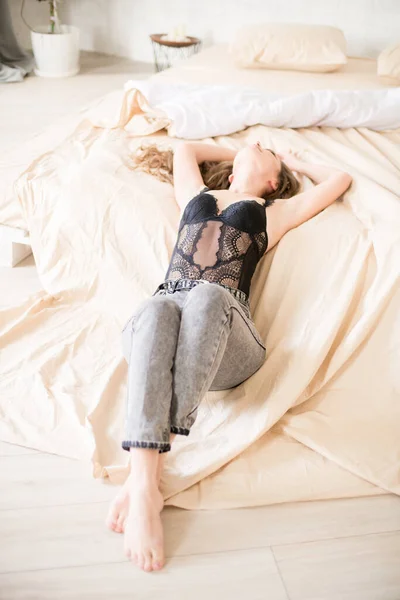 청바지를 곱슬머리의 매력적 침실에 침대에 레이스가 티셔츠 — 스톡 사진