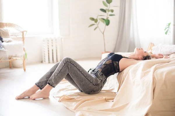청바지를 곱슬머리의 매력적 침실에 침대에 레이스가 티셔츠 — 스톡 사진