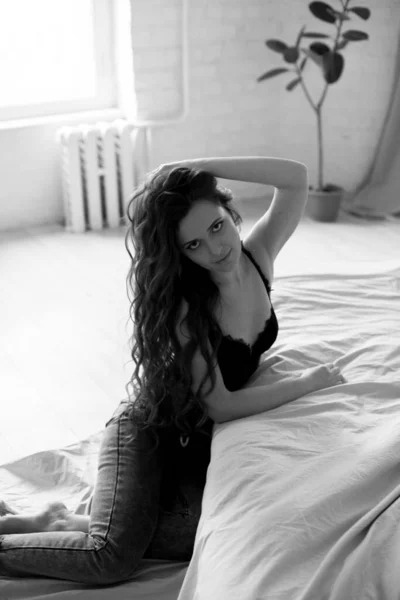 Uzun Kıvırcık Saçlı Kot Pantolonlu Yatakta Dantelli Siyah Tişörtlü Çekici — Stok fotoğraf