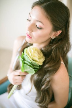 Stüdyoda bir buket çiçekli, beyaz elbiseli, uzun saçlı, Asyalı tatlı genç gelin.