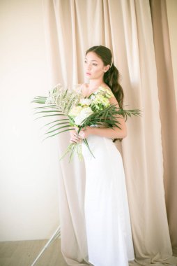 Stüdyoda bir buket çiçekli, beyaz elbiseli, uzun saçlı, Asyalı tatlı genç gelin.