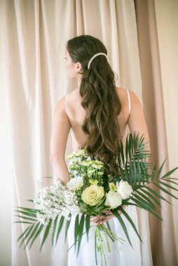 Stüdyoda bir buket çiçekli, beyaz elbiseli, uzun saçlı, Asyalı tatlı genç gelin.