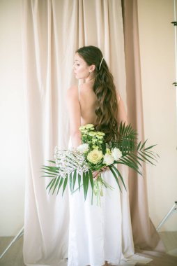 Stüdyoda bir buket çiçekli, beyaz elbiseli, uzun saçlı, Asyalı tatlı genç gelin.