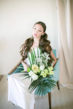Stüdyoda bir buket çiçekli, beyaz elbiseli, uzun saçlı, Asyalı tatlı genç gelin.