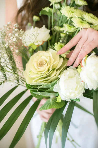 Delicate wedding bouquet in a rustic style of white flowers with green leaves in the hands of the bride