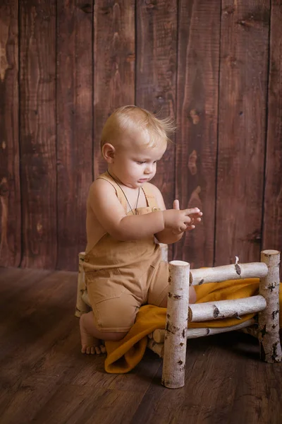 금발의 귀여운 아기는 어두운 배경에 자작나무 가지로 침대를 가지고 것이다 — 스톡 사진