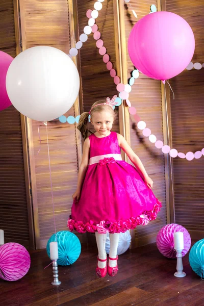 Little cute girl with blond hair in a pink dress and a princess crown with large bright balloons and garlands. Children\'s holiday. Children\'s decor. Balloons