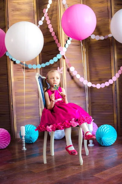 Little cute girl with blond hair in a pink dress and a princess crown with large bright balloons and garlands. Children's holiday. Children's decor. Balloons