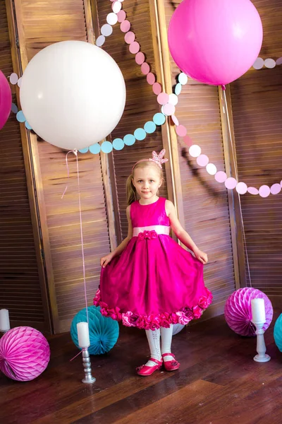 Little cute girl with blond hair in a pink dress and a princess crown with large bright balloons and garlands. Children\'s holiday. Children\'s decor. Balloons