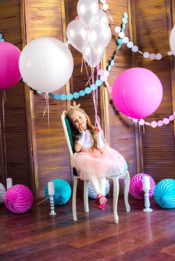 Pembe elbiseli, sarı saçlı küçük şirin kız ve büyük parlak balonları ve çelenkleri olan prenses tacı. Çocuk tatili. Çocuk dekoru. Balonlar