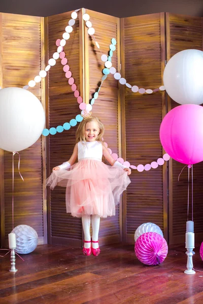一个可爱的小女孩 金发碧眼 穿着粉红的衣服 头戴公主王冠 戴着大大的明亮的气球和花环 儿童节 儿童的装饰 — 图库照片