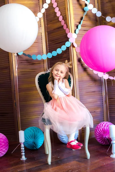 Little cute girl with blond hair in a pink dress and a princess crown with large bright balloons and garlands. Children\'s holiday. Children\'s decor. Balloons