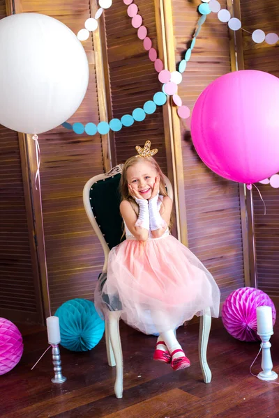 Little cute girl with blond hair in a pink dress and a princess crown with large bright balloons and garlands. Children's holiday. Children's decor. Balloons