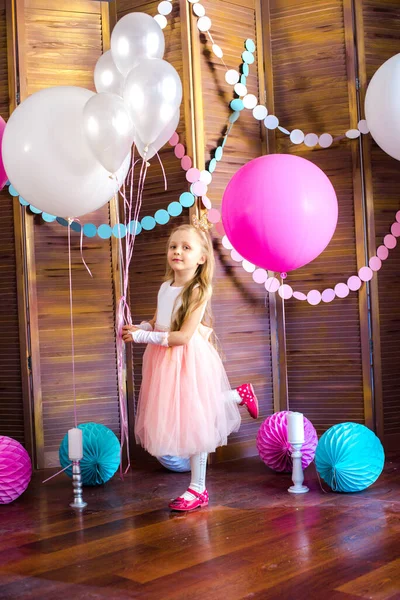 Little cute girl with blond hair in a pink dress and a princess crown with large bright balloons and garlands. Children\'s holiday. Children\'s decor. Balloons