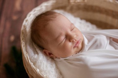 Hasır sepetin içinde beyaz bir battaniyenin içinde, tahta zeminde iğne dalları ve pamukla süslenmiş şirin bir bebek. Mutlu annelik
