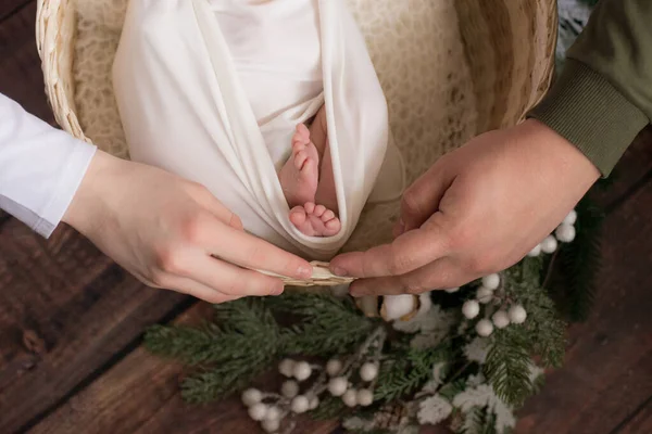 爸爸妈妈的手把可爱的小宝宝的腿放在一个白色的毯子里 放在一个柳条篮里 上面装饰着针叶树的枝条和地板上的棉花 母性快乐 — 图库照片