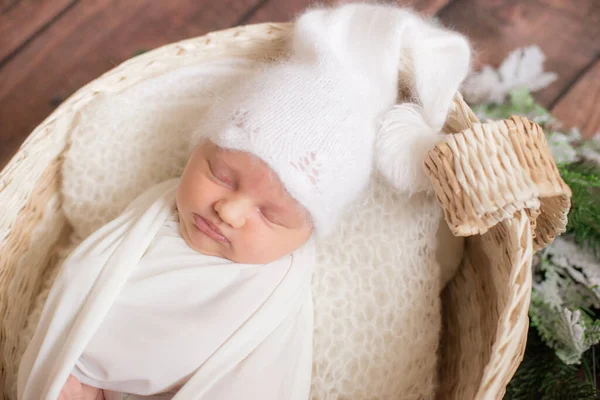 穿着白色毛毯的可爱小宝宝 戴着白色针织帽子 头戴柳条篮 用针枝和棉花装饰在木制地板上 母性快乐 — 图库照片
