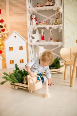 Sarı saçlı şirin çocuk, Noel ağacının yanında süslenmiş parlak bir odada ahşap eko oyuncaklarla oynuyor. Mutlu bir çocukluk. Noel havası