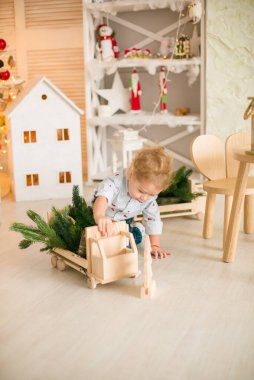 Sarı saçlı şirin çocuk, Noel ağacının yanında süslenmiş parlak bir odada ahşap eko oyuncaklarla oynuyor. Mutlu bir çocukluk. Noel havası