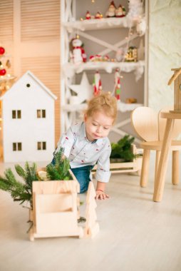 Sarı saçlı şirin çocuk, Noel ağacının yanında süslenmiş parlak bir odada ahşap eko oyuncaklarla oynuyor. Mutlu bir çocukluk. Noel havası
