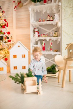 Sarı saçlı şirin çocuk, Noel ağacının yanında süslenmiş parlak bir odada ahşap eko oyuncaklarla oynuyor. Mutlu bir çocukluk. Noel havası