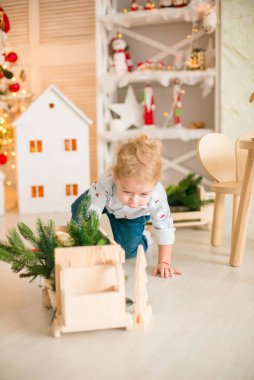 Sarı saçlı şirin çocuk, Noel ağacının yanında süslenmiş parlak bir odada ahşap eko oyuncaklarla oynuyor. Mutlu bir çocukluk. Noel havası