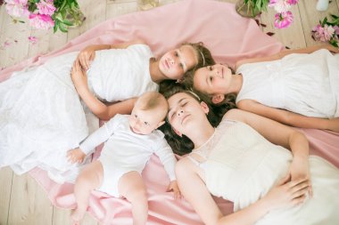 Tatlı çocuklar, beyaz elbiseli küçük bir erkek kardeş ve ablalar pembe şakayıklı parlak bir bahar stüdyosunda yerde birlikte yatıyorlar. Mutlu bir aile. Mutlu çocukluk