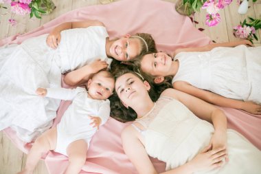 Tatlı çocuklar, beyaz elbiseli küçük bir erkek kardeş ve ablalar pembe şakayıklı parlak bir bahar stüdyosunda yerde birlikte yatıyorlar. Mutlu bir aile. Mutlu çocukluk