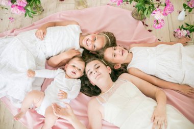 Tatlı çocuklar, beyaz elbiseli küçük bir erkek kardeş ve ablalar pembe şakayıklı parlak bir bahar stüdyosunda yerde birlikte yatıyorlar. Mutlu bir aile. Mutlu çocukluk