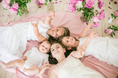 Tatlı çocuklar, beyaz elbiseli küçük bir erkek kardeş ve ablalar pembe şakayıklı parlak bir bahar stüdyosunda yerde birlikte yatıyorlar. Mutlu bir aile. Mutlu çocukluk